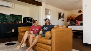 A room with a brown leather sofa, a kitchen area with a black refrigerator, a coffee table, and a small round table with a cup. - The Wesley Hotel (Page)