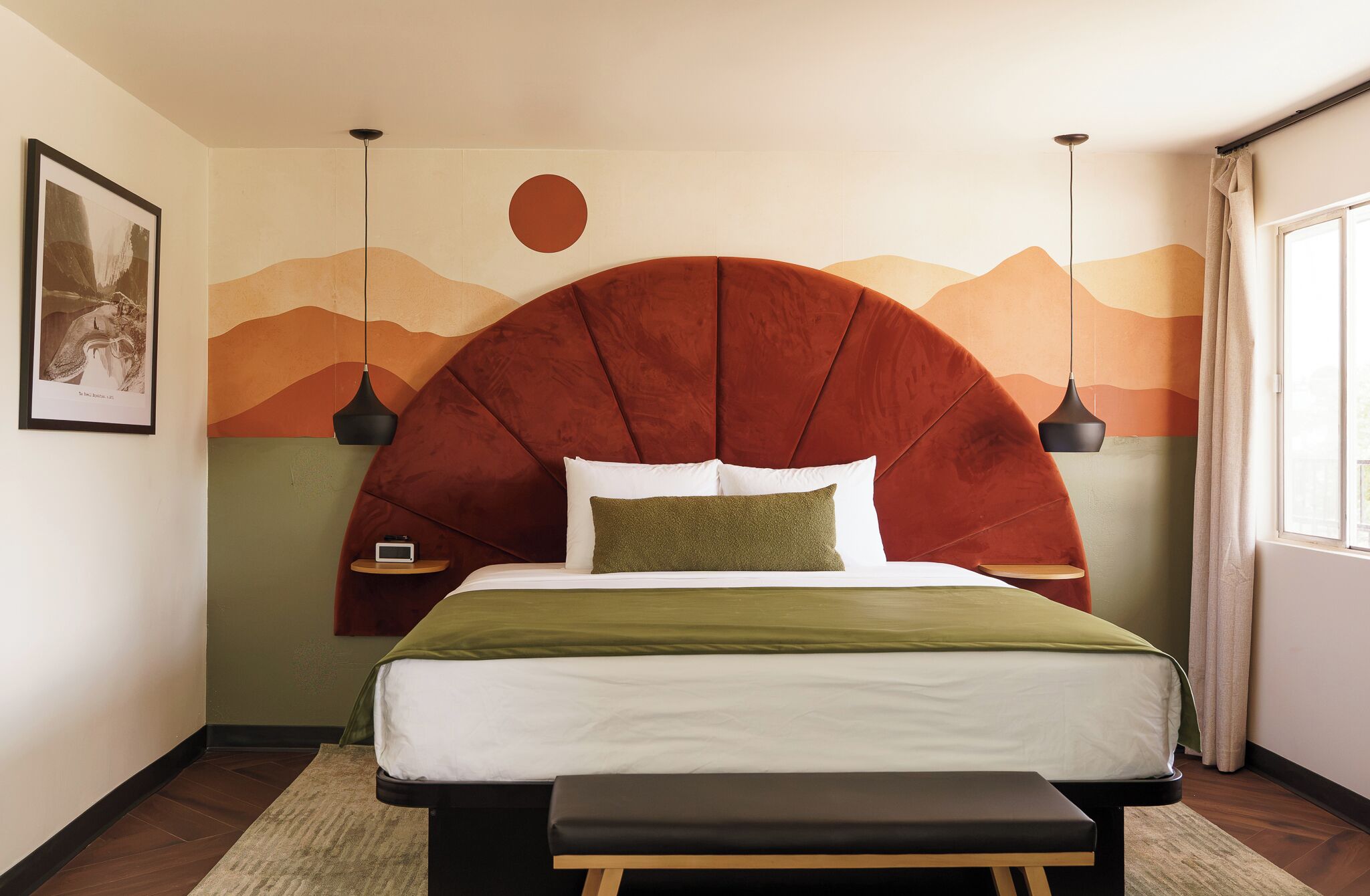 Un dormitorio con una cama grande, cabecera de diseño circular, mesitas de noche y una obra de arte colgada en la pared.