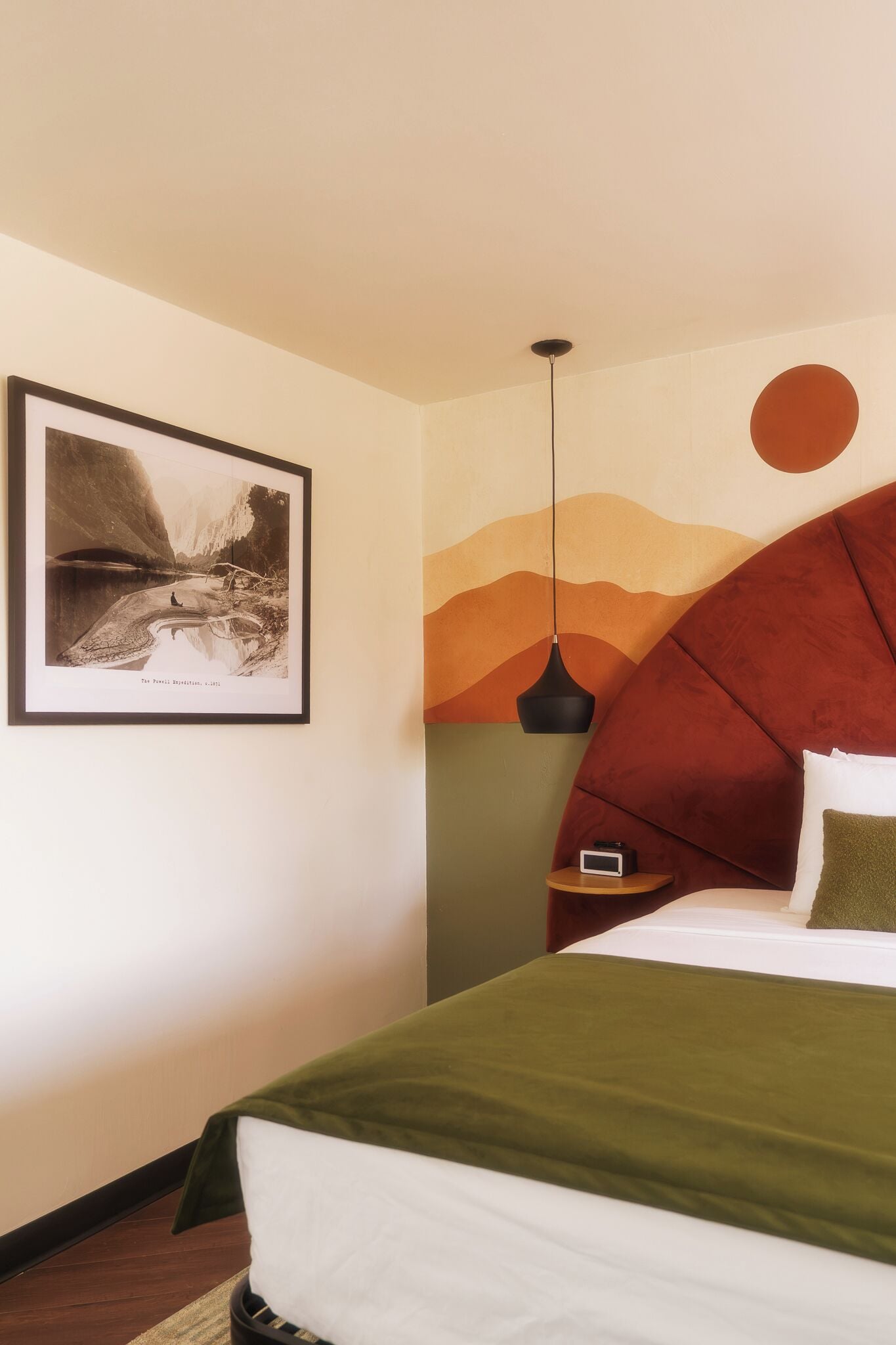 Un dormitorio con una cama, un cuadro enmarcado en la pared, una lámpara colgante y un mural.