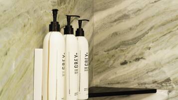 A bathroom with marble walls, a white towel, and three bottles of Grey+ hand soap.