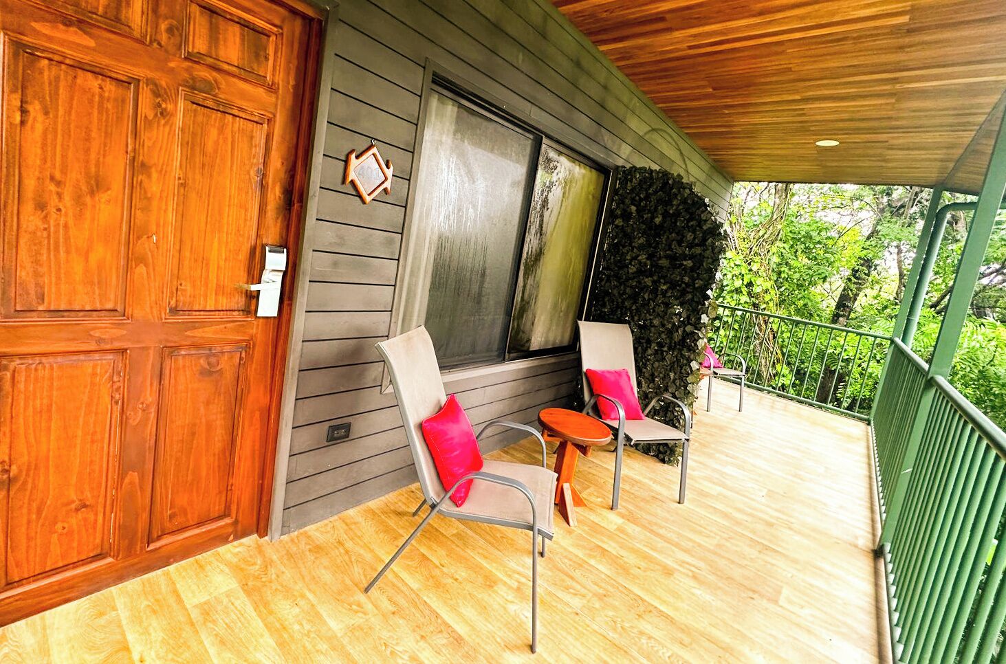 A wooden deck with two chairs and a table, a large wooden door, and a stone wall.