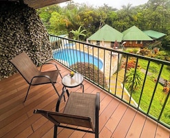 A wooden deck with two chairs and a table, a pool, and a view of a building with green roofs.
