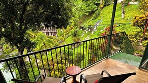 A balcony with two chairs and a small table, overlooking a lush garden and a building. - Tabulia Tree Hotel and Villas (Quepos)