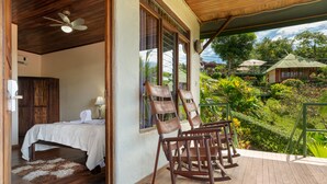 A wooden deck with rocking chairs, a bed with a white bedspread, and a view of lush greenery. - Tabulia Tree Hotel and Villas (Quepos)