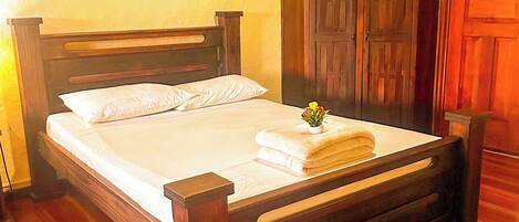 A wooden bed with white linens, a nightstand, a wooden wardrobe, and a wall-mounted light fixture.