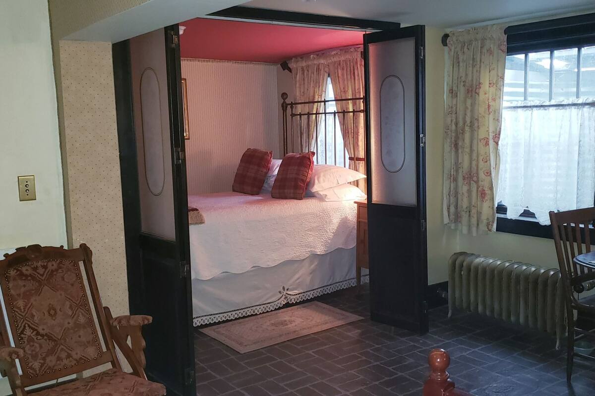 Un dormitorio con cama, una silla, una mesa y una ventana con cortinas.