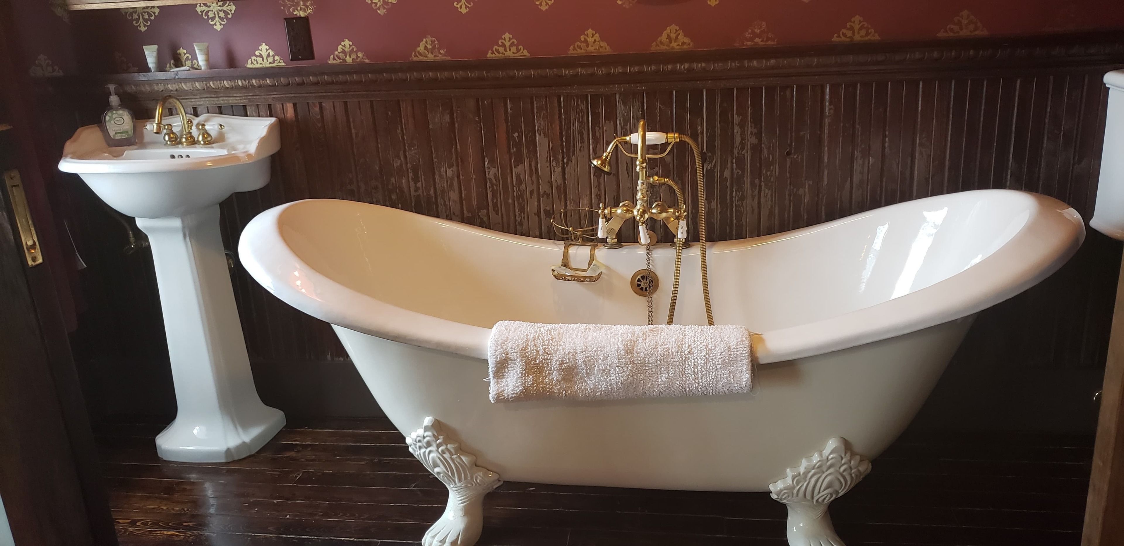 A classic clawfoot bathtub with a towel, a pedestal sink, and ornate wall decorations.