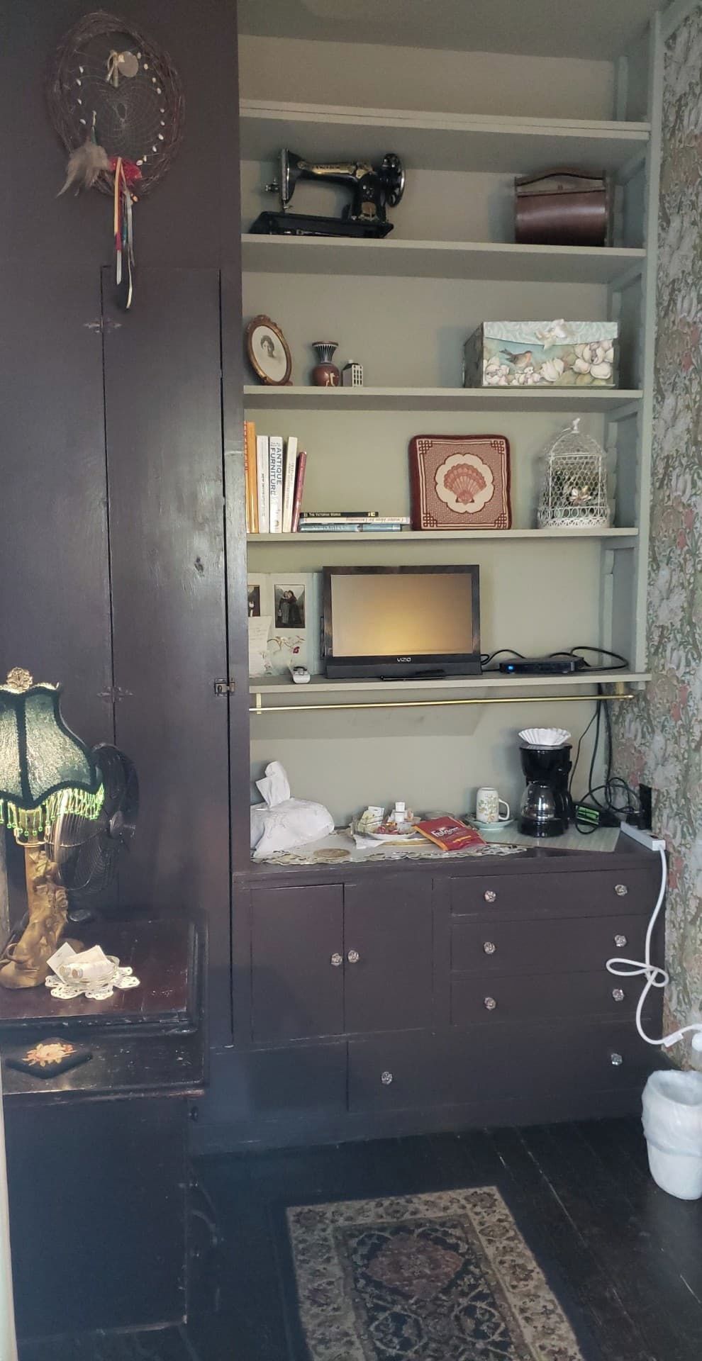 Una habitación con un mueble de madera oscura, una máquina de coser, un televisor y varios objetos decorativos en estantes.