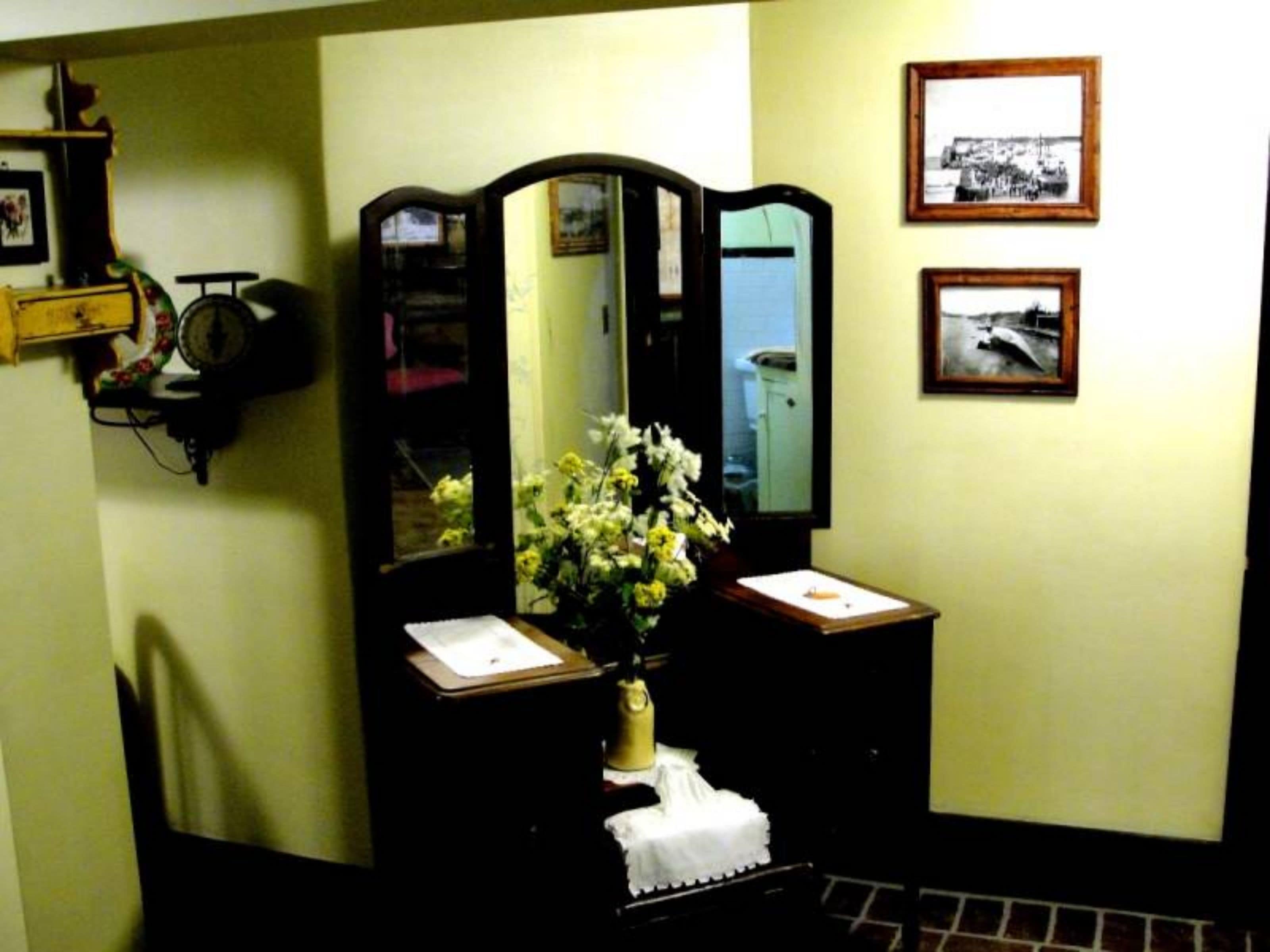 A room with a mirror, a vase with flowers, and two framed pictures on the wall.