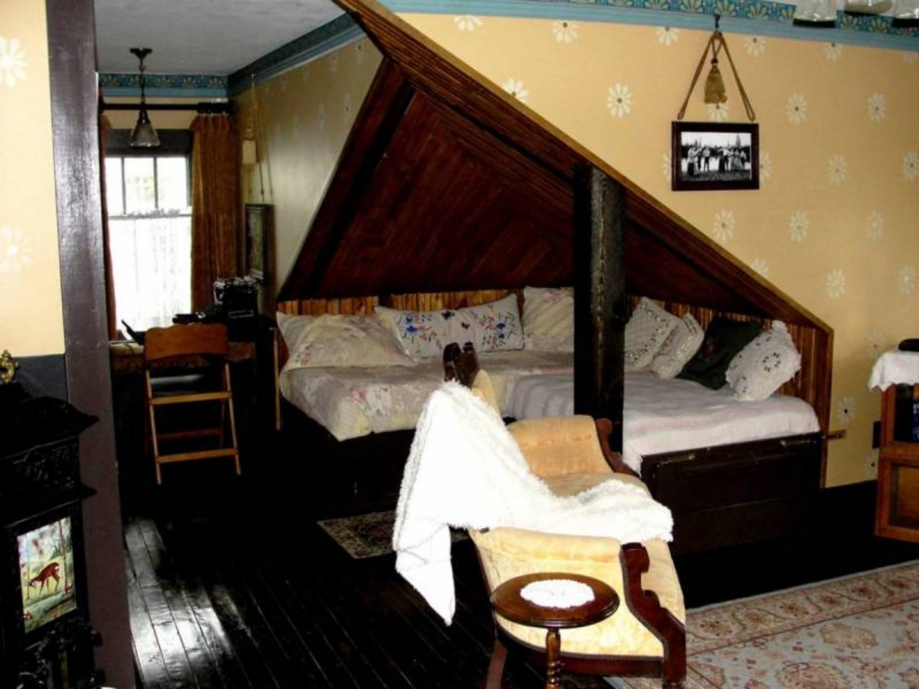 Ein Zimmer mit schrägem Dach, einem Bett mit Holz Kopfteil, einem kleinen Tisch mit einer Schale und einer Hängelampe.