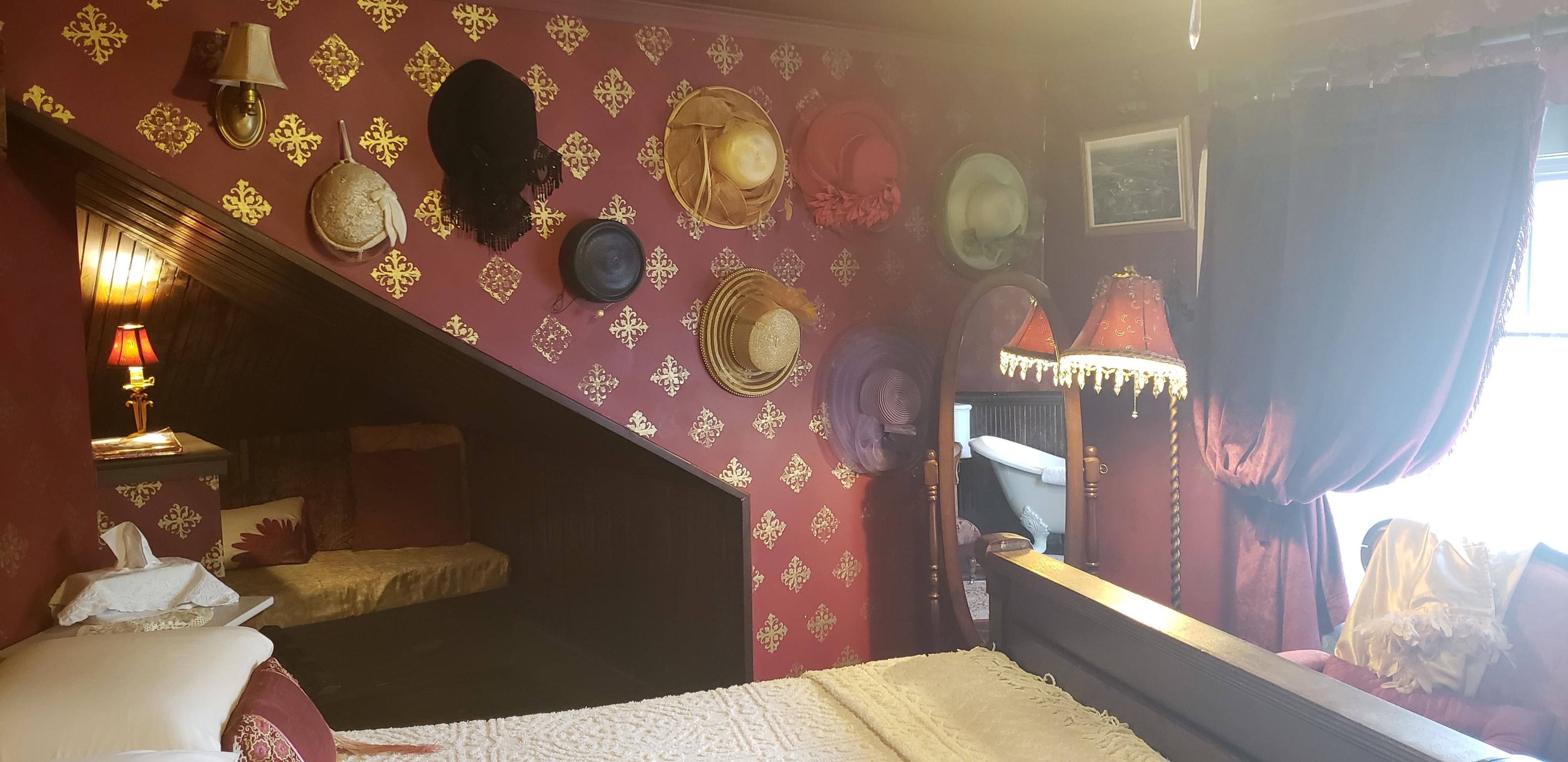 Une pièce avec un escalier, un lit, un miroir et divers chapeaux accrochés au mur.