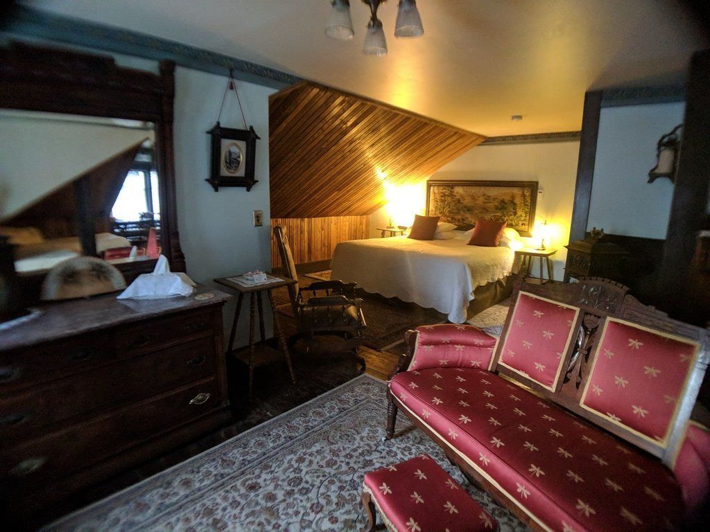 Ein Zimmer mit einem Bett, einem Holzschrank, einem rot gepolsterten Sofa und einem gemusterten Teppich.