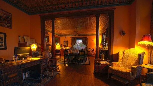 A traditional room with a wooden floor, a desk with a lamp, a patterned armchair, and a dining area with chairs and a table.