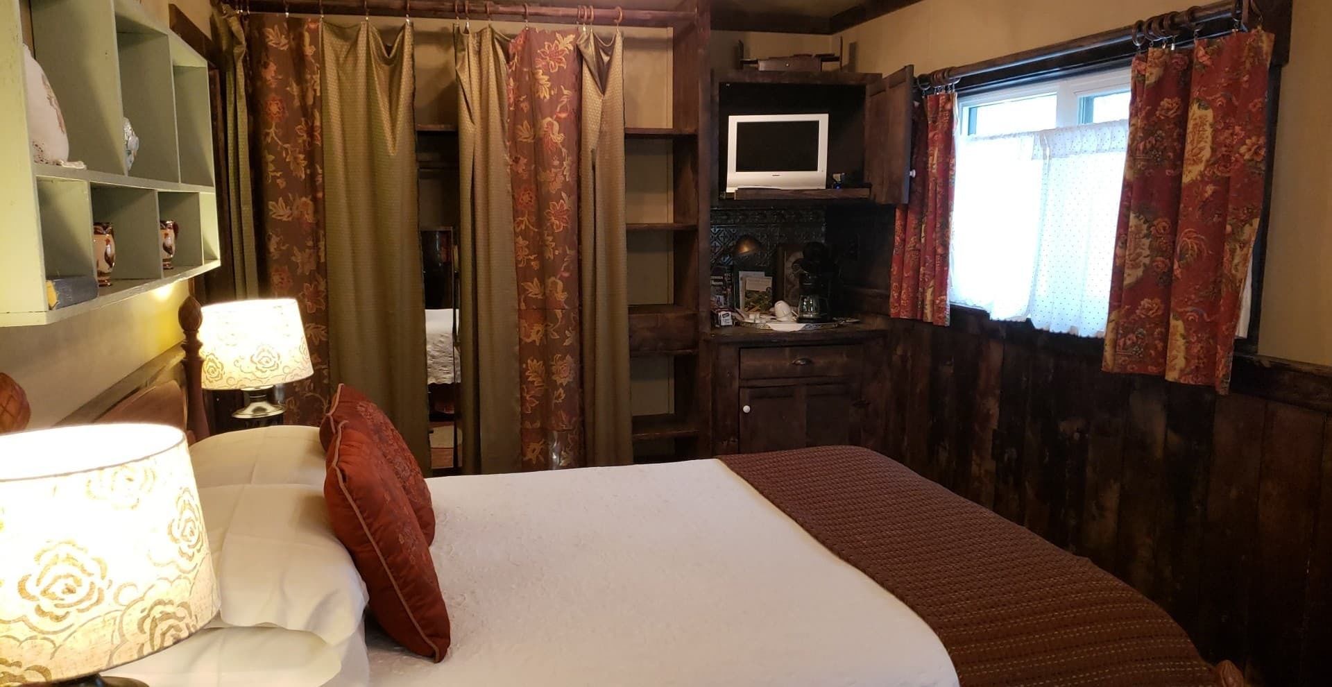A hotel room with a bed, a desk, a television, and a wardrobe.