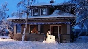 A two-story house with a snow-covered roof and a snowman sculpture in front.