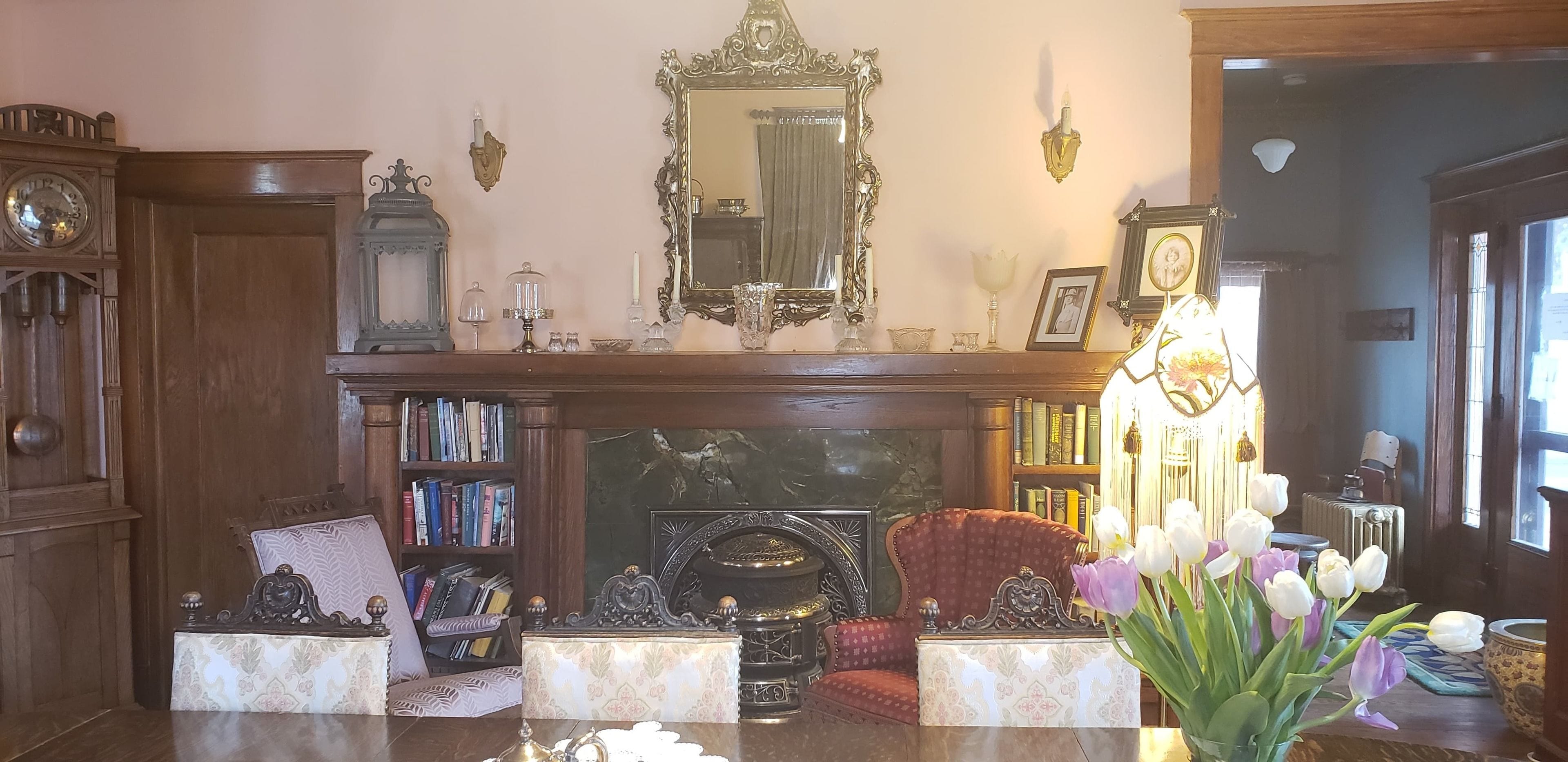 Uma biblioteca tradicional com lareira, estantes de livros, uma poltrona vermelha e um vaso de tulipas.