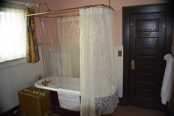 A bathroom with a bathtub, a shower curtain, a radiator, and a door. - Alaska Heritage House Bed and Breakfast (Fairbanks)