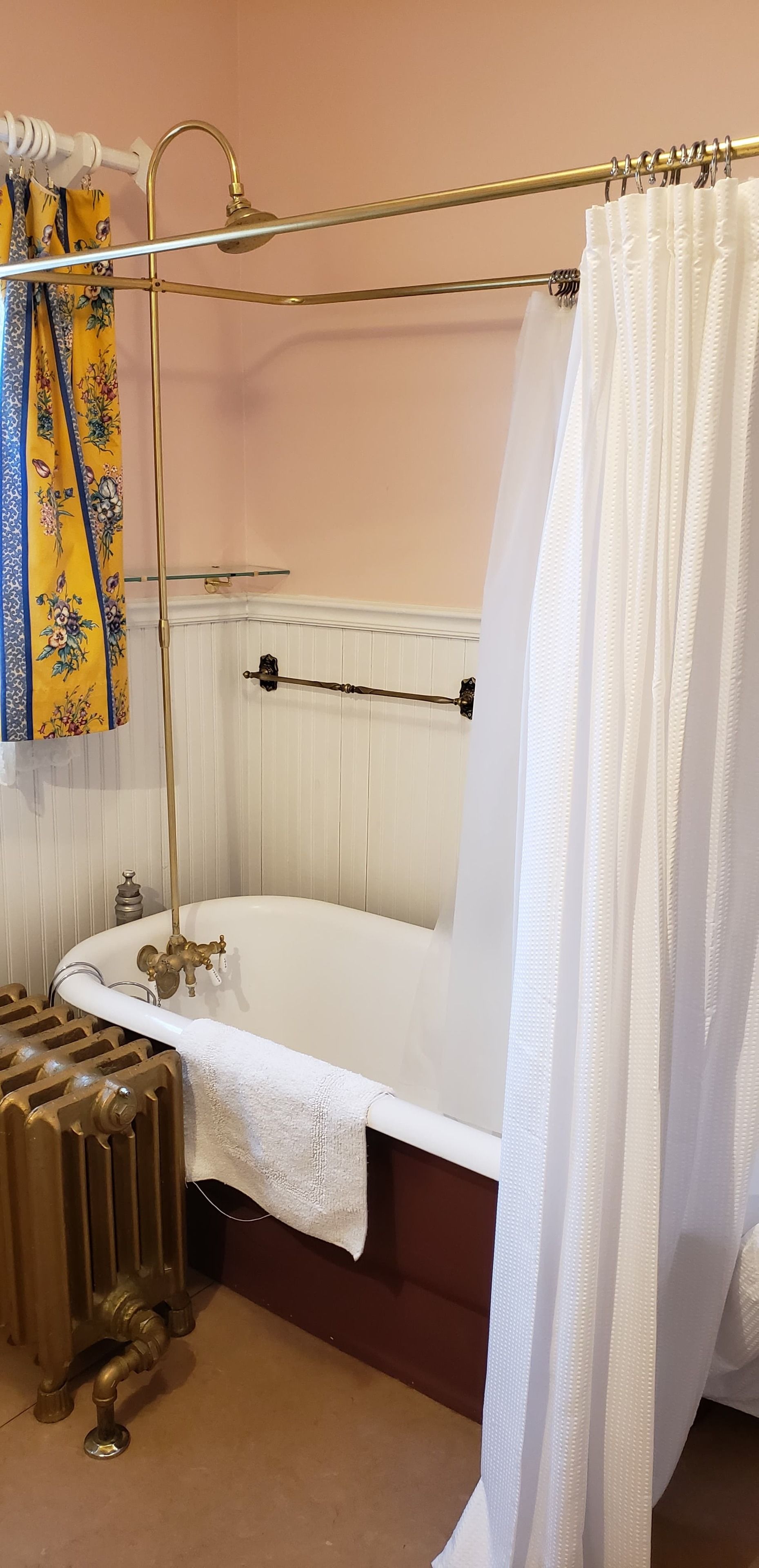A bathroom with a freestanding bathtub, a radiator, and a curtain rod with a white curtain.