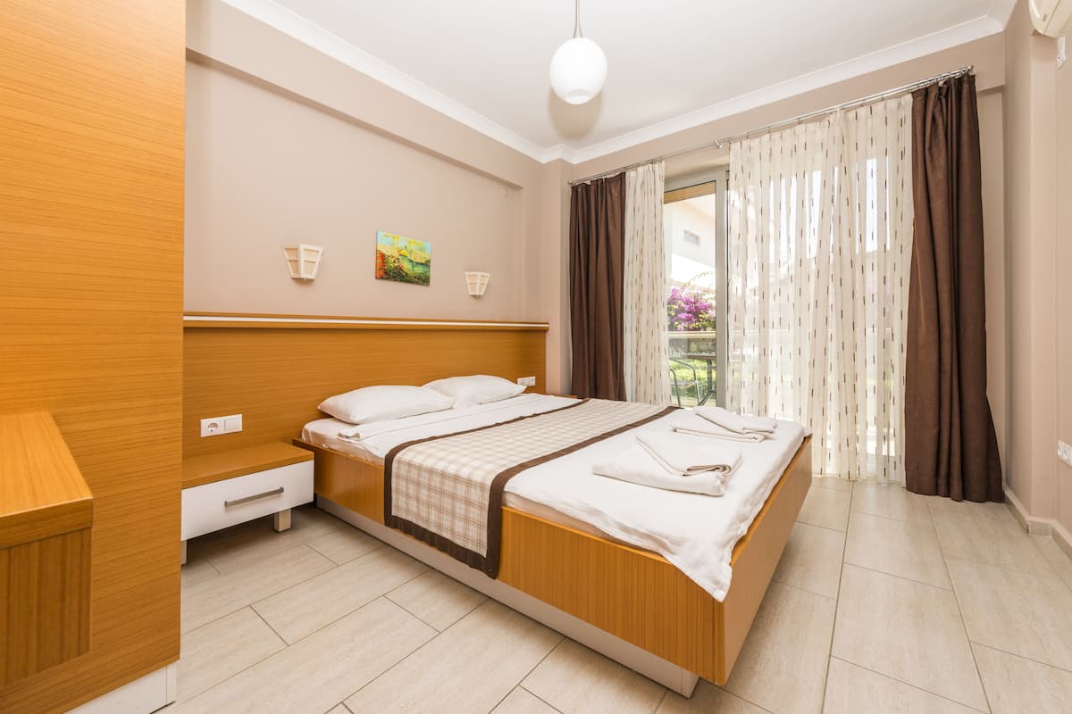 Un dormitorio moderno con una cama de madera, una mesita de noche y vistas al exterior a través de cortinas traslúcidas.