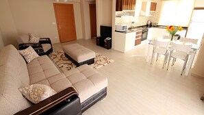 A living room with a sofa, ottoman, and a dining area with a table and chairs. - Diana Residence (Fethiye)