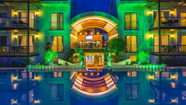 A multi-story hotel with a central courtyard, balconies, and a pool reflecting the building. - Diana Residence (Fethiye)