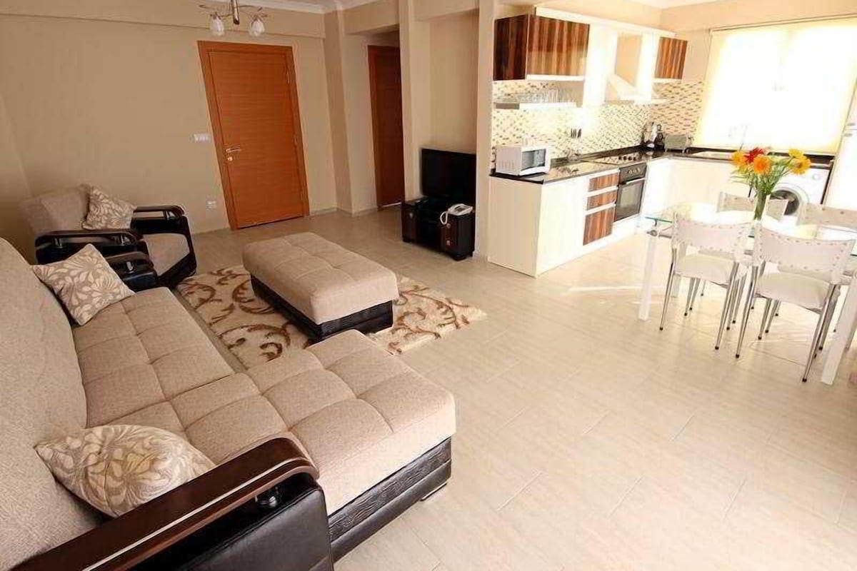 A modern living room with a sofa, ottoman, and a dining area with chairs.