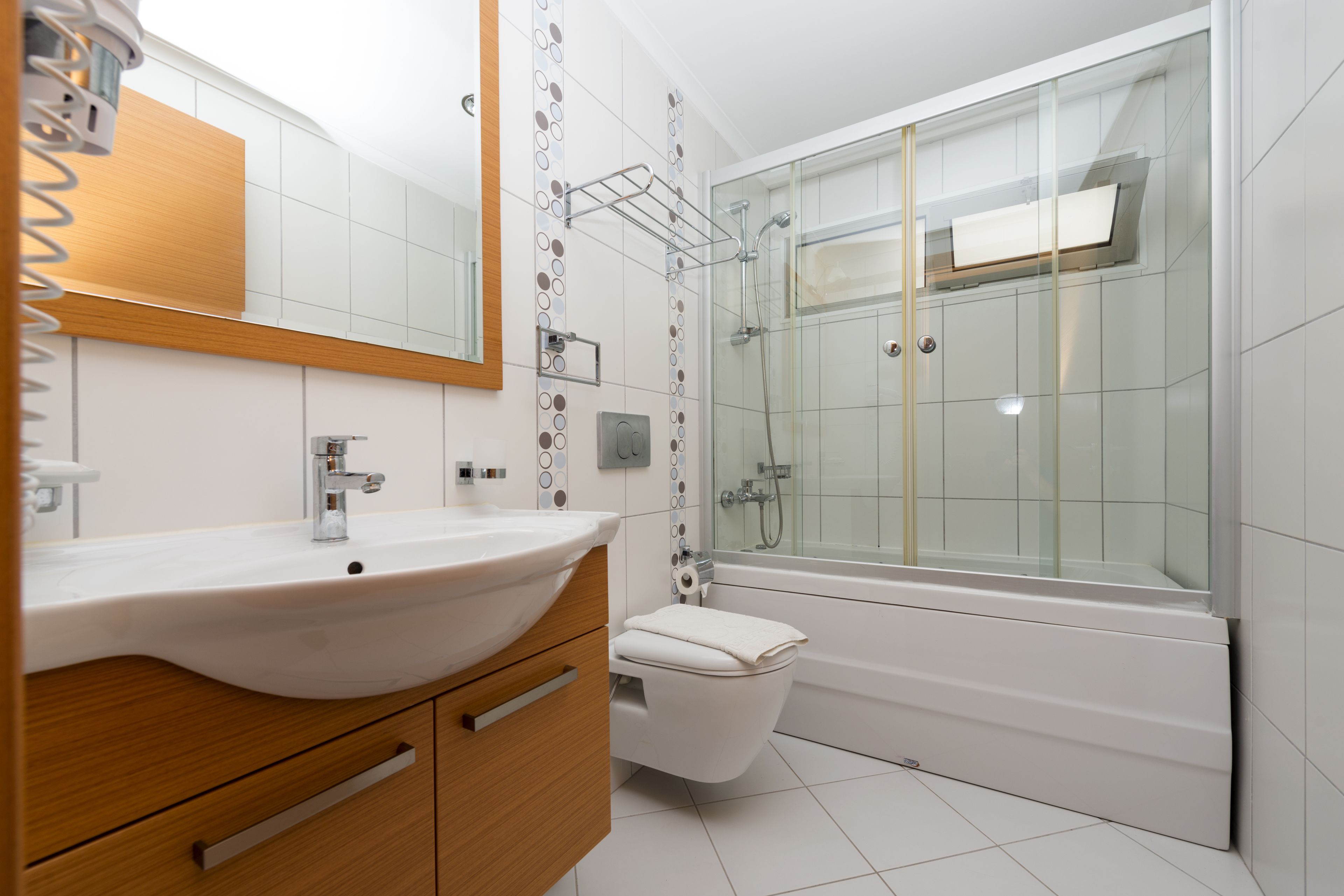 Une salle de bain moderne avec un lavabo blanc, un meuble-lavabo en bois, une cabine de douche en verre et des toilettes blanches.