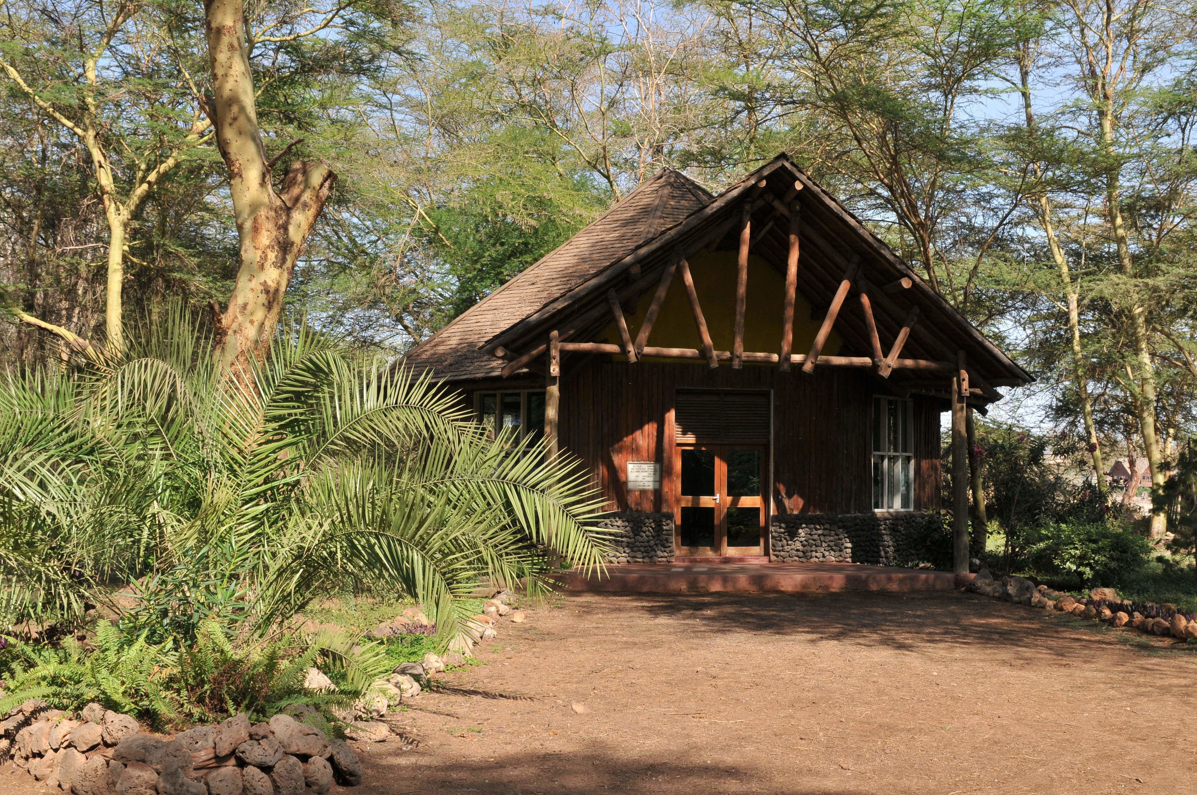 A rustic wooden cabin with a pitched roof, surrounded by lush greenery and trees.