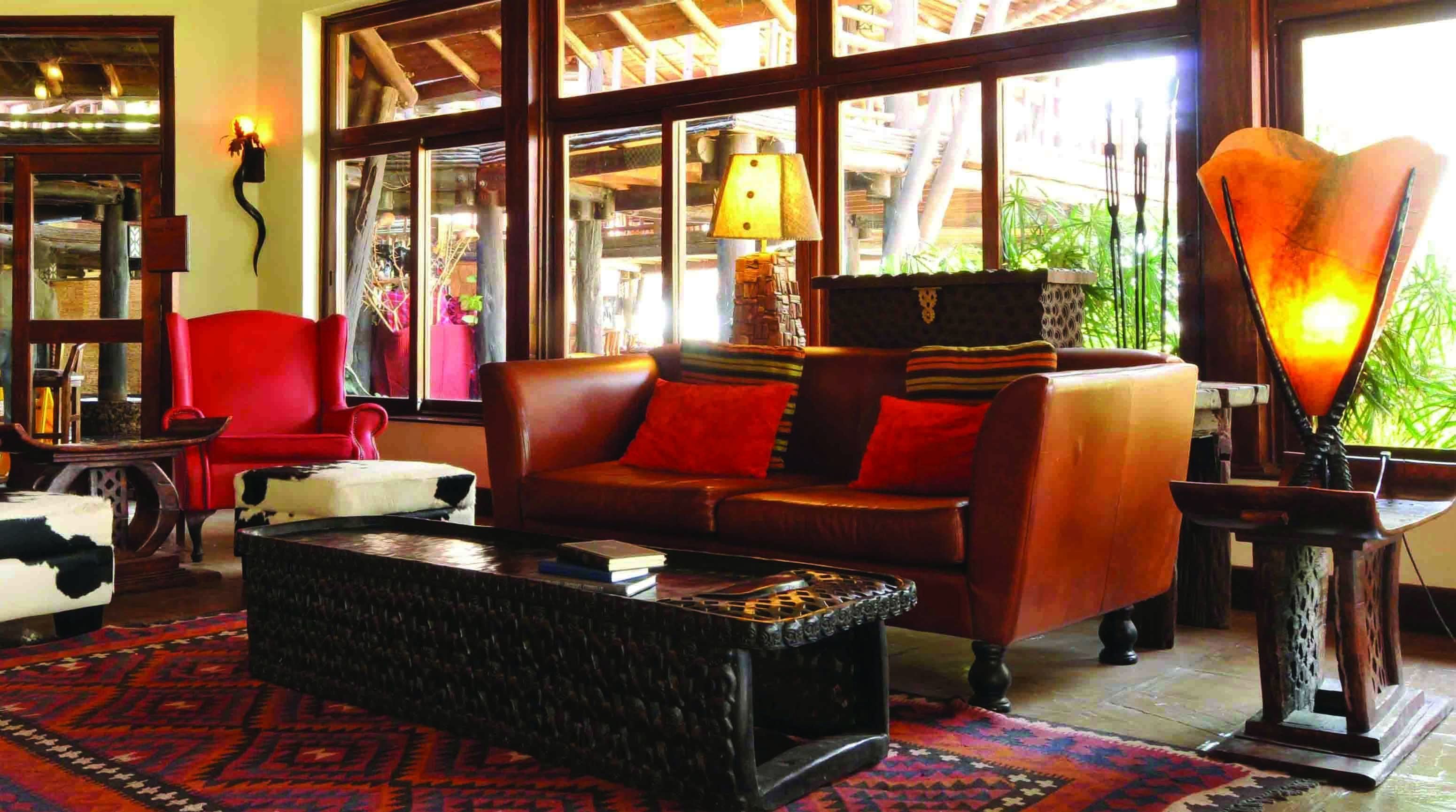 Una sala de estar acogedora con un sofá de cuero marrón, cojines rojos, una mesa de centro negra y una alfombra estampada.