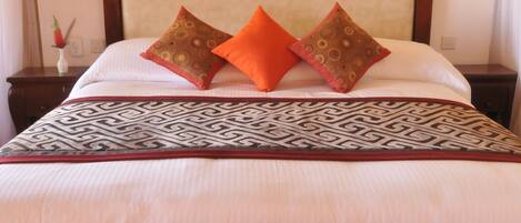 Una habitación de hotel con una cama grande, dos lámparas fijadas a la pared, una pared de acento roja y una manta decorativa estampada.