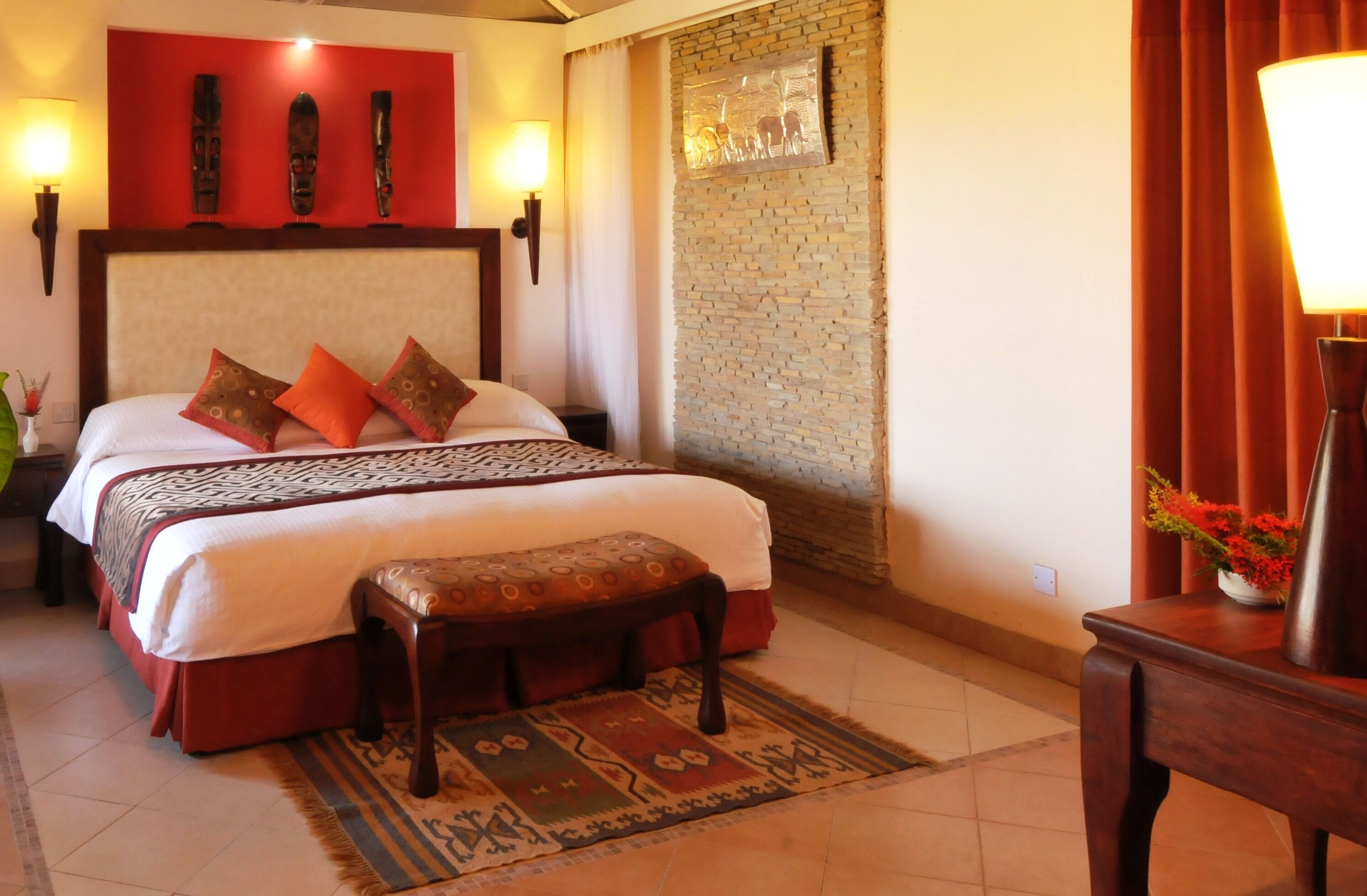 Habitación de hotel con una cama grande, cabecera de madera, una banca, alfombra y pared con diseño de ladrillo.