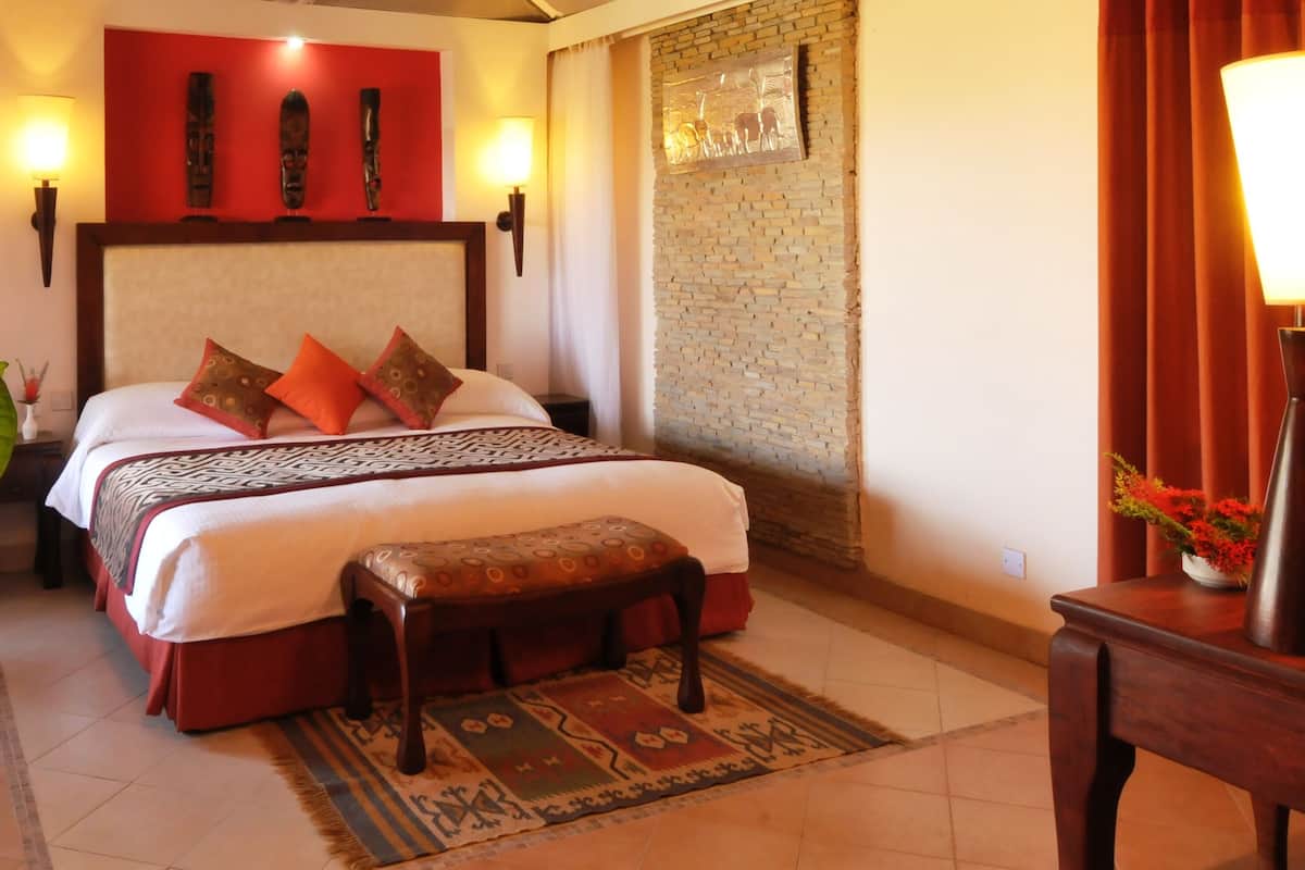 A hotel room with a large bed, a wooden headboard, a bench, a rug, and a wall with a brick pattern.