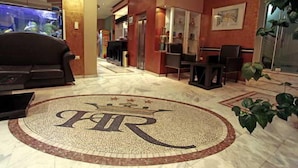 Eine Hotelhalle mit kreisförmigem Wappen, einer Sitzgelegenheit und einer Rezeption.