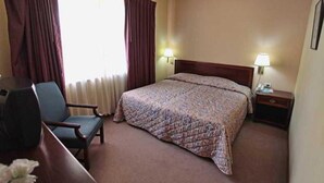 Ein Hotelzimmer mit einem Bett, einem Sessel, einem Schreibtisch und einem Nachttisch mit Lampe.