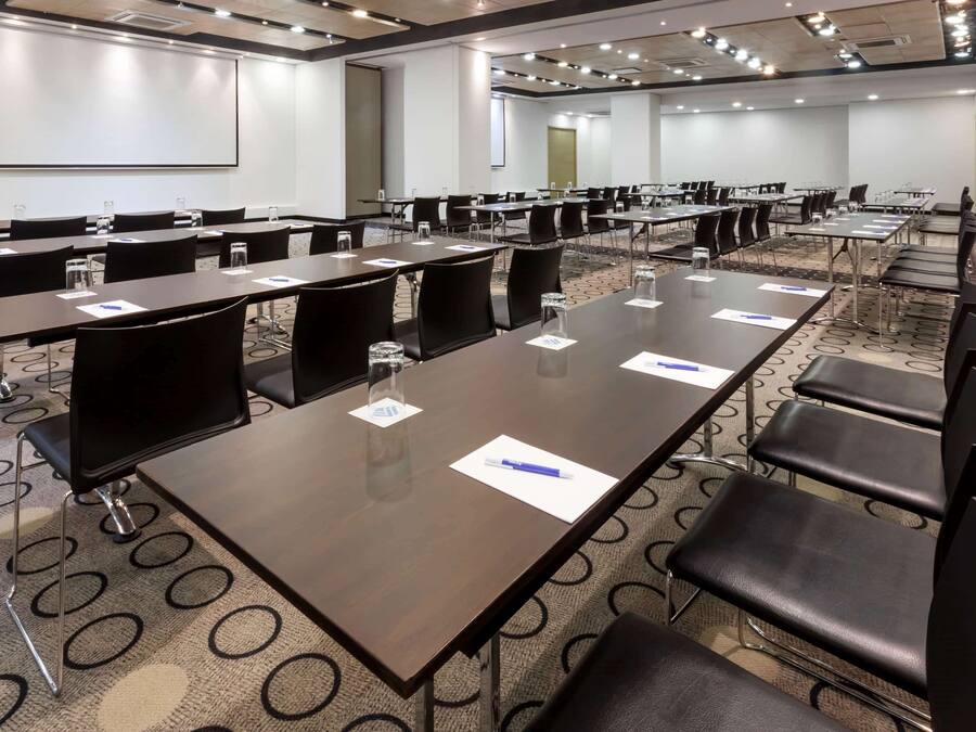 Un salón de conferencias con varias mesas y sillas, equipado con botellas de agua y tarjetas de nombre.