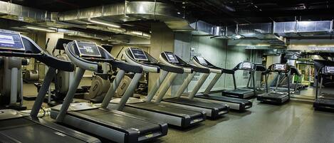 A row of treadmills in a gym with visible control panels and overhead lighting.