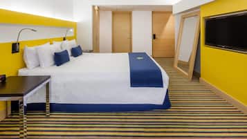A hotel room with a bed, a desk, a chair, a TV, and a door.