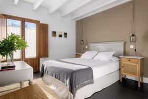 Quarto com cama, mesa de cabeceira e planta em vaso.