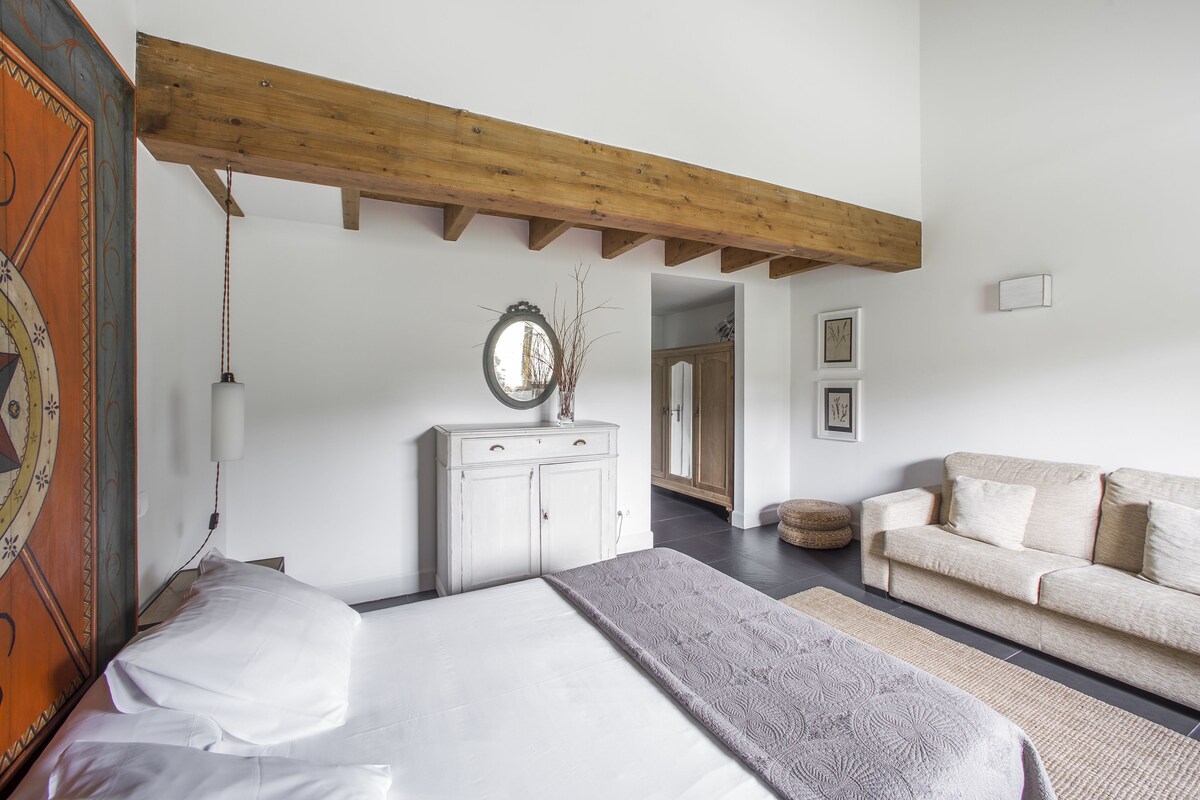 Une chambre à coucher comprenant un lit, une commode, un canapé et une poutre en bois au plafond.