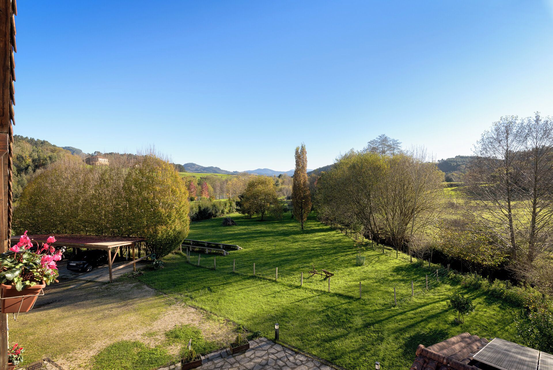 Un giardino curato con una pergola in legno, vista libera sulle colline circostanti e area recintata.