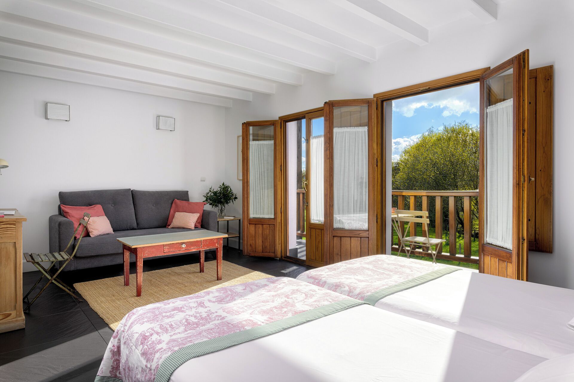 A bedroom with a bed, a sofa, a small table, and a balcony with a wooden railing.