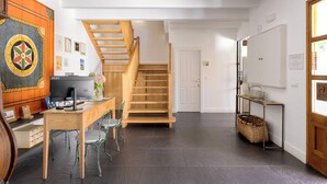 Un intérieur moderne avec un escalier en bois, un bureau avec un ordinateur et une porte blanche portant l’inscription « WC ».
