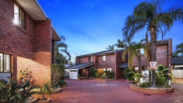 A brick building with a paved driveway, palm trees, and a speed limit sign.