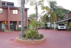A courtyard with a brick building, palm trees, and a white SUV parked nearby.