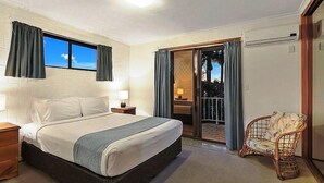A bedroom with a bed, bedside tables, a chair, a window with curtains, and a sliding glass door leading to a balcony.