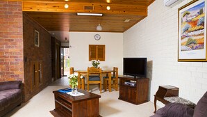 A living room with a wooden ceiling, brick walls, a television, a dining table with chairs, and a sofa.