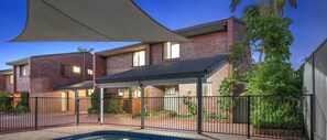 A residential building with a covered patio, brick exterior, and a swimming pool.