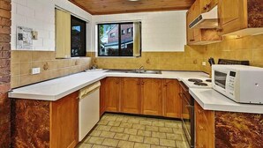 A compact kitchen with wooden cabinets, a white countertop, a built-in microwave, and a window with a view of buildings outside.