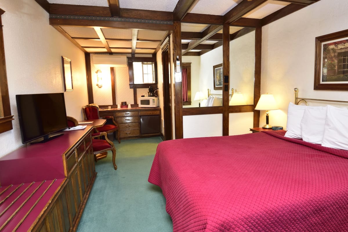 A hotel room with a bed, a desk, a television, a mirror, and a painting on the wall.