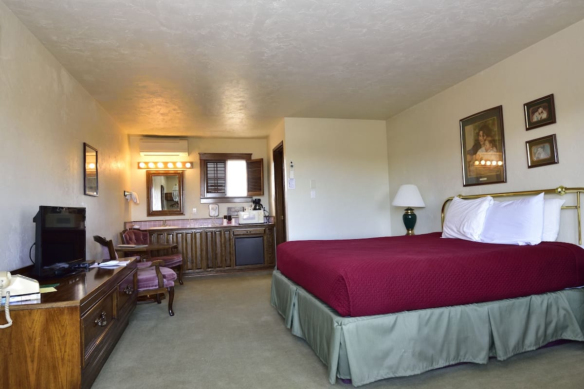 A hotel room with a bed, bedside table, lamp, dresser, desk with a telephone, and a mirror.